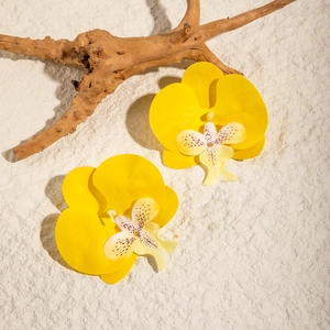 Close-up of yellow orchid earrings with purple spotted centers on a textured stone surface
