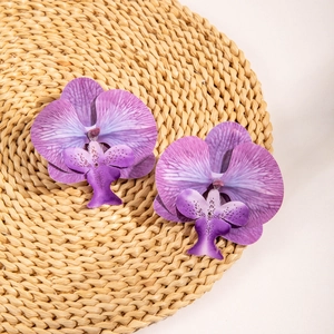 Close-up of 3D orchid earrings with purple gradient petals on a woven texture mat