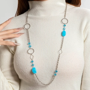 Detail van een lange boho-ketting met blauwe kralen en zilveren ketting op witte trui
