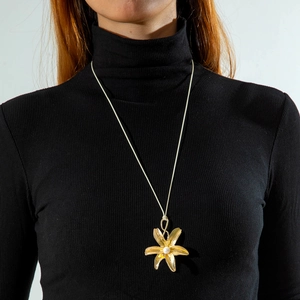 Detail van een gouden bloem hanger met parel op een zwarte trui ketting voor dames