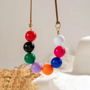 Detail van een lange boho-ketting met kleurrijke harskralen en gouden verbindingen