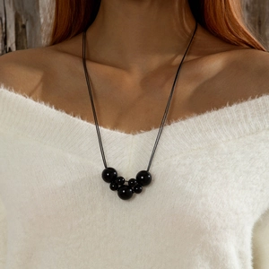 Detail van een lange zwarte kralenketting met bloemhanger op een witte trui