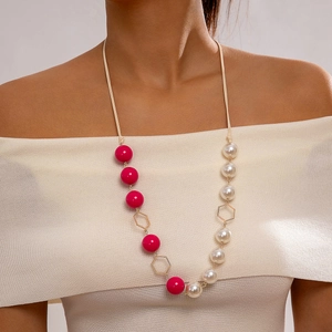 Detail van de lange ketting met roze kralen en parels op een beige gebreide trui