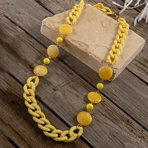 Macrodetail van amberkleurige kralen en gele matte schakels op een lange ketting
