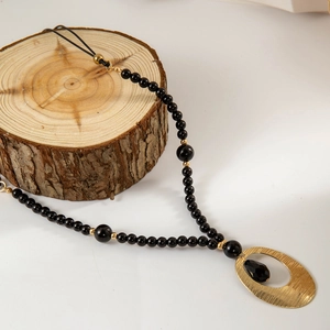 Detail van kralenketting met gouden hanger met textuur en zwarte gefacetteerde steen