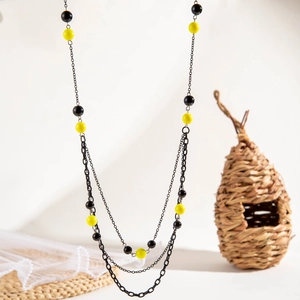 Detail van een lange gelaagde ketting met zwarte en neongele kralen op een gevlochten mat