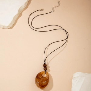Detail van een amberbruine hars hanger met marmertextuur en zwart waskoord met sluiting