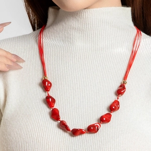 Detailopname van een lange modeketting met rode onregelmatige kralen en goudaccenten