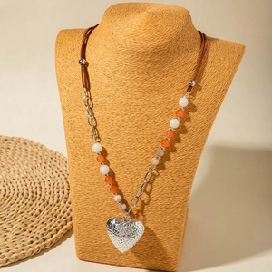 Detail van een gelaagde lange ketting met een grote hartvormige hanger op een geweven buste