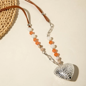 Detail van zilveren hartvormige hanger aan lange kralenketting met bruin lederen koord