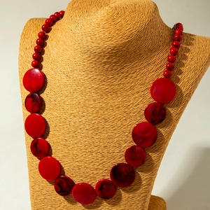 Detail van lange rode hars kralenketting met gemarmerde hanger op een getextureerde halsdisplay