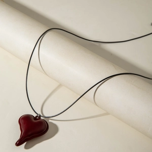 Detail van een dieprode artistieke hartvormige hanger met een minimalistisch zwart koord