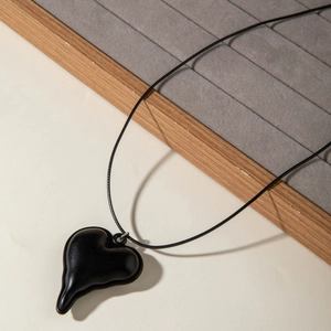 Detail van een minimalistische zwarte hartvormige hanger met glanzende afwerking en koord