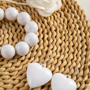 Set bracciale di perle bianche e orecchini a cuore su un tappeto intrecciato