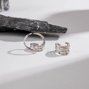 Close-up of irregular silver hollow curved ring set on white stone surface