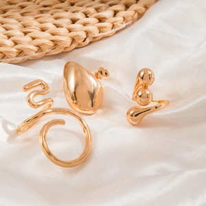 Detailed view of three gold irregular open rings on a white silk and straw background