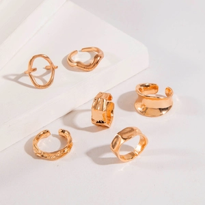 Detailed view of six gold-tone irregular hollow curved rings on a white geometric stand