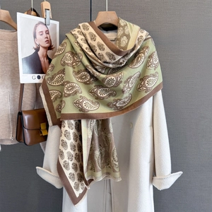 Green and brown paisley print scarf with fringe edges styled on a white coat