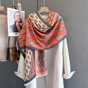 Detail of paisley print scarf with fringe edge draped over a white wool coat