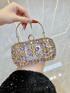 Close-up of luxury evening bag with purple and amber crystals and a round metal handle