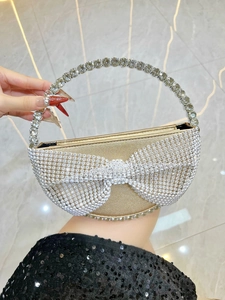 Detail of gold evening clutch featuring a sparkling rhinestone bow and circular jeweled handle