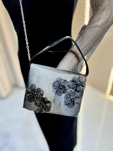 Détail de pochette de soirée en satin argenté avec fleurs en dentelle et chaîne fine