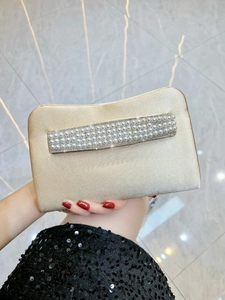 Close-up of champagne silk satin evening bag with rows of pearls and rhinestones
