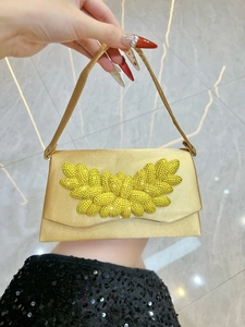 Detailed shot of champagne gold satin evening clutch with radiant yellow rhinestone leaf