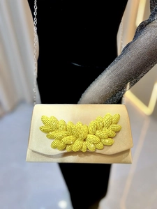 Detailed macro of champagne satin evening bag featuring a yellow rhinestone jewel cluster