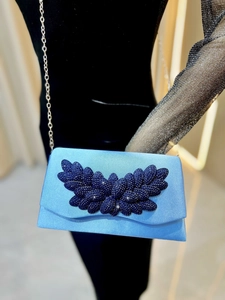 Detail of light blue satin clutch bag with deep blue rhinestone leaf pattern and silver chain