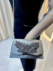 Macro detail of silver clutch bag with black bead leaf pattern and metal chain