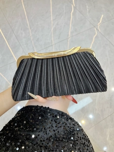Detail of black pleated evening clutch bag with gold rhinestone clasp held by hand