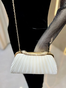 Detail of white pleated evening clutch with gold metal frame and rhinestone trim
