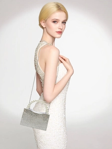 Close-up of sparkling rhinestone clutch with pearl handle worn by model in white dress