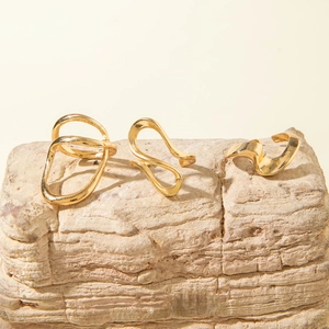 Detailed view of three minimalist gold-plated irregular wave rings on natural stone