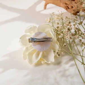 Detailed back view of a creamy fabric camellia hair clip with a silver metal duckbill base
