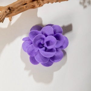 Detail of purple fabric camellia hair clip showing layered petals on gray background