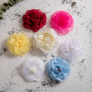 Colorful chiffon camellia flower hair clips in seven shades on a textured background