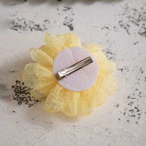 Detail of yellow fabric camellia hair clip with metal crocodile clamp on textured base