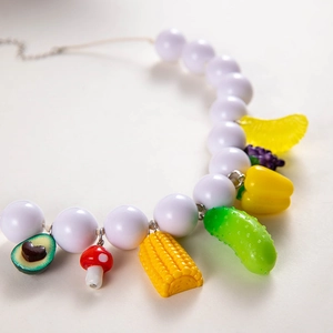 Close-up of white beaded necklace featuring colorful fruit and vegetable charms