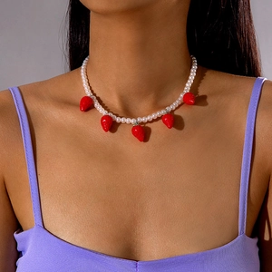 Detailed view of white pearl necklace with five red strawberry pendants on model