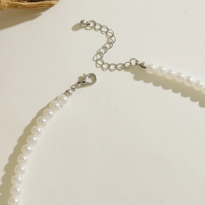 Detail of white beaded necklace showing silver lobster clasp and extension chain on white surface