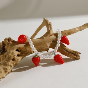Detail of white faux pearl bracelet with cute red strawberry pendants on a wooden branch