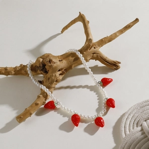 Detailed view of white pearl necklace with red strawberry pendants on a wooden branch