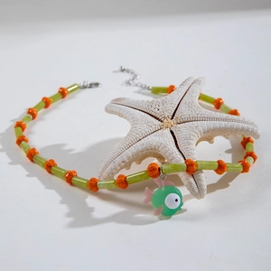 Detail of bohemian beaded necklace with green fish charm and vibrant orange star beads