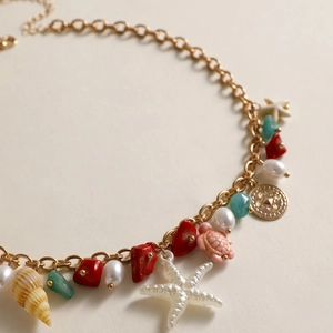 Detail of gold chain necklace with white pearl, starfish, seashell, and turtle charms