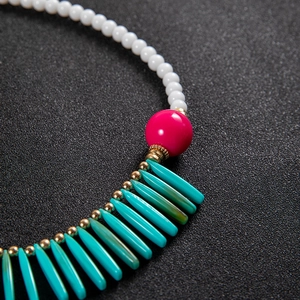 Détail d'un collier bohème avec perles blanches, perle rouge rose et segments turquoise