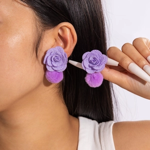 Detail showing elegant purple fabric rose and soft plush pompom drop earrings on model