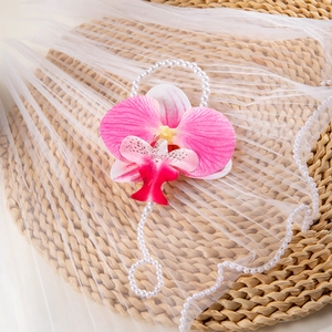 Macro detail of 3D printed pink orchid and pearls on a straw mat with white tulle