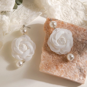 Détail de boucles d'oreilles rose en tissu avec perles et ruban sur pierre rose